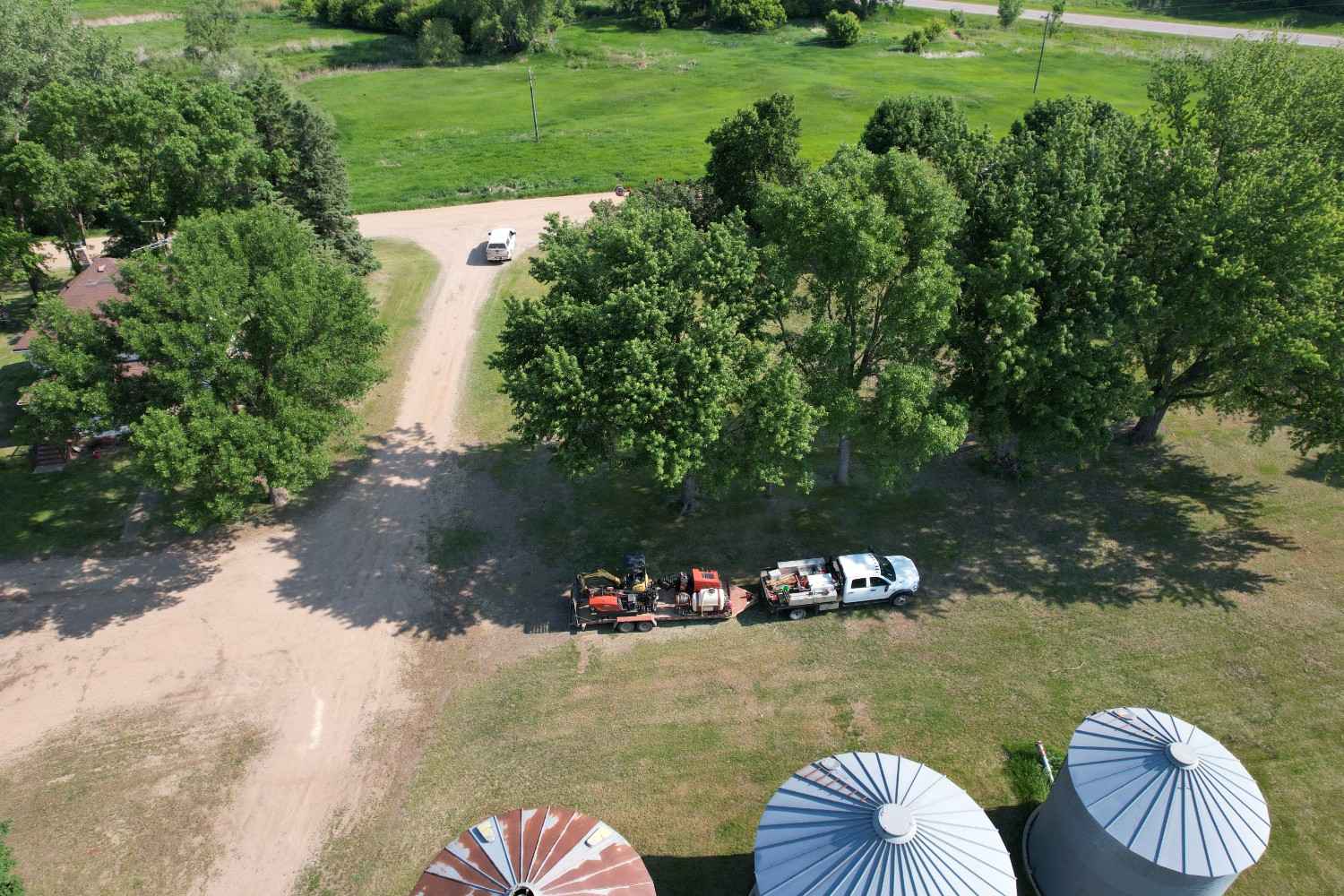 Hide wood fiber crew equipment staged near farm grain bins and trees.
