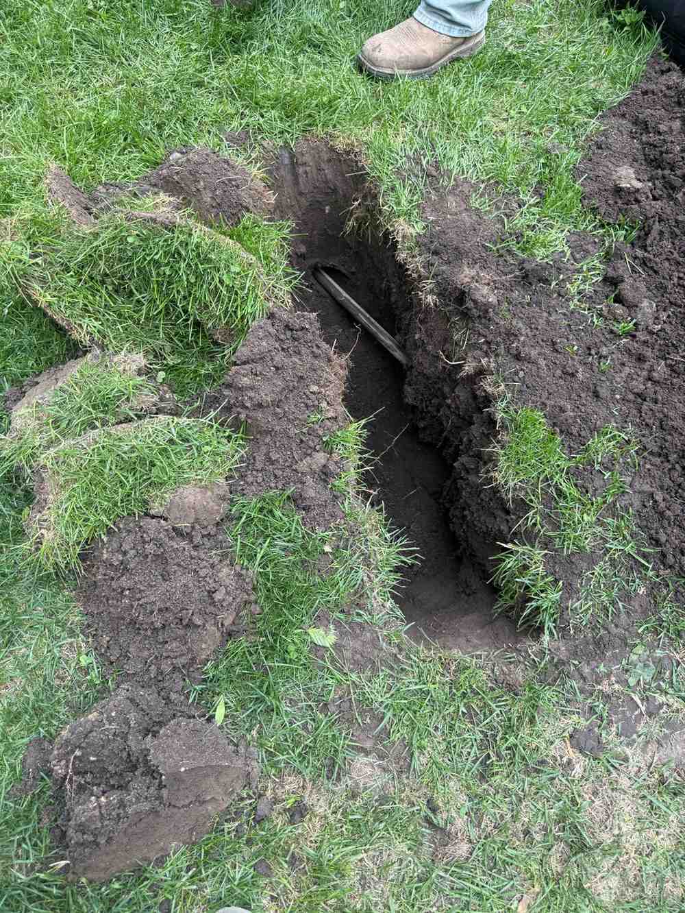 Small trench showing buried fiber cable installed in a residential lawn.